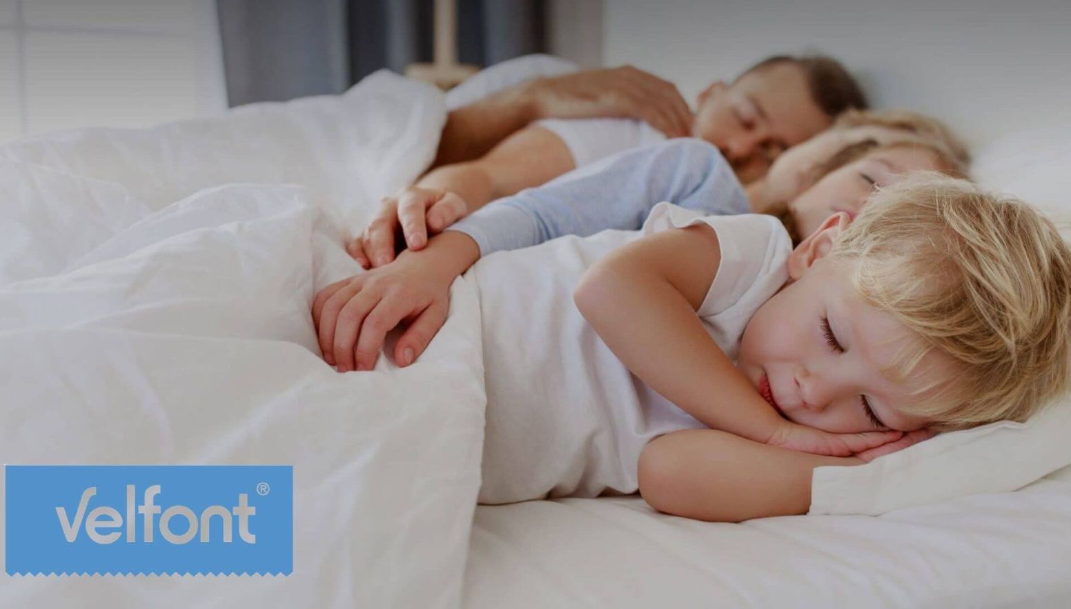 Familia descansando en una cama con ropa de cama blanca - Velfont